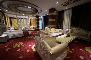 Habitación de hotel con cama, dos sofás, una mesa de centro y alfombra estampada.