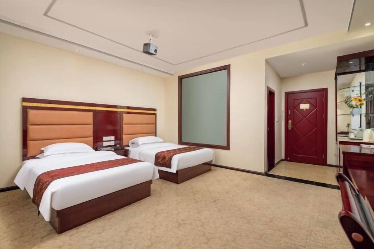 Hotellihuone, jossa on kaksi sänkyä, suuri peili, punainen ovi ja pieni työpöytä.