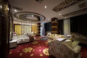 Una habitación de hotel con cama, sofá, mesa de centro y techo decorado.