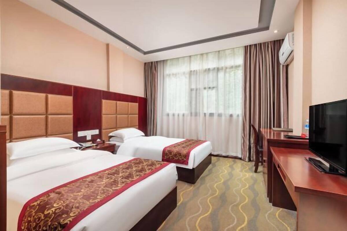 Hotellihuone, jossa on kaksi sänkyä, työpöytä, televisio ja ikkuna, jossa on verhot.