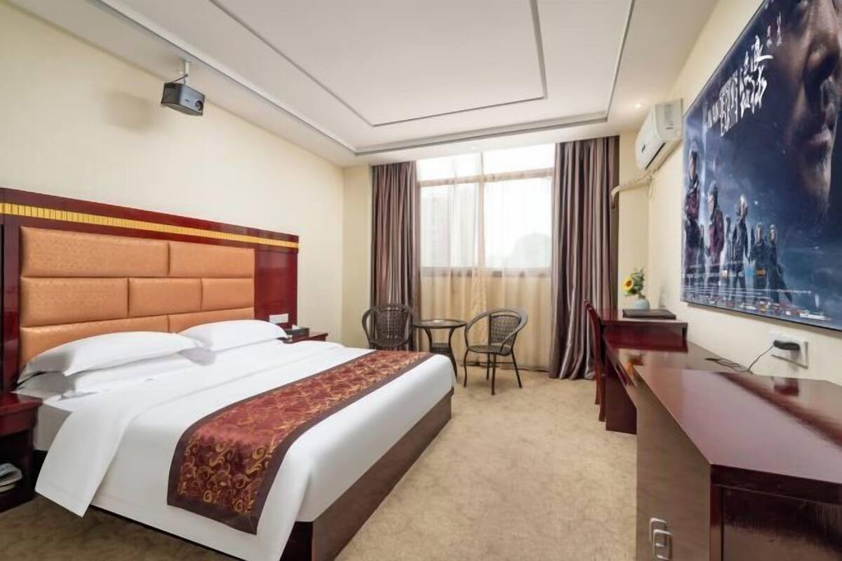 Hotellihuone, jossa on suuri sänky, työpöytä, tuoli, pieni pöytä ja televisio.
