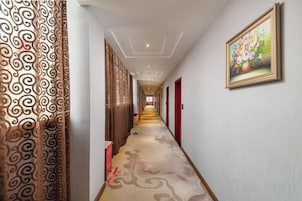 Un pasillo de hotel con cortinas estampadas, un cuadro floral en la pared y suelo alfombrado.