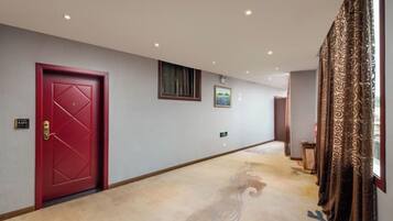 A hotel hallway with a red door, a carpeted floor, and a window with curtains.