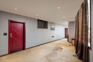 Un pasillo de hotel con una puerta roja, suelo alfombrado y una ventana con cortinas.