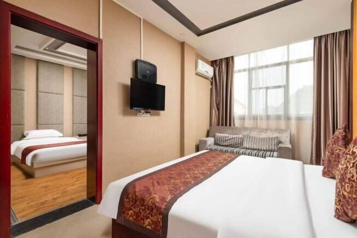Hotellihuone, jossa on suuri sänky, seinälle asennettu televisio ja ikkuna, jossa on verhot.