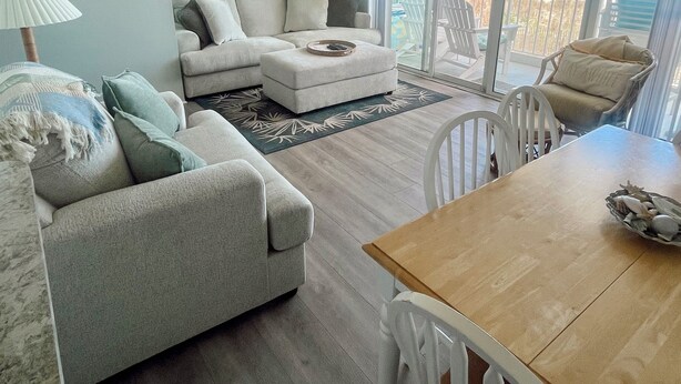 A living room with a sofa, ottoman, and a dining table with chairs. - NEW Beautiful Ocean Front Condo with Private Balcony and Beach Access (Ocean City)