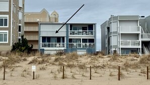 A beachfront building with multiple balconies and a sandy foreground. - NEW Beautiful Ocean Front Condo with Private Balcony and Beach Access (Ocean City)
