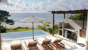 An infinity pool with lounge chairs, a pergola, and a view of the ocean. - Villa Pietro | Beachfront 2BR Villa w Pool (Sayulita)
