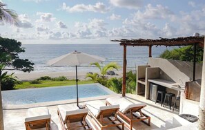 Une piscine à débordement avec des chaises longues, une pergola et une vue sur l’océan.