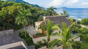 A coastal property with a thatched-roof house, lush greenery, and a view of the sea.