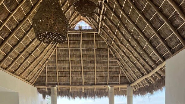 A dining area with a thatched roof, wooden chairs, and a table set for a meal.