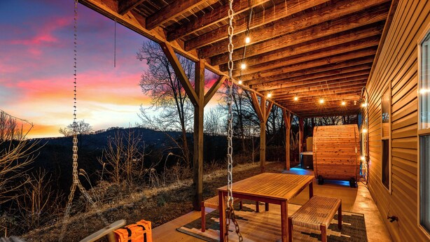 Une terrasse en bois avec une balançoire, une table et un banc.