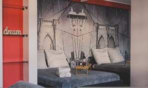 A hotel room with a large cityscape mural on the wall, two beds with pillows, a small table with a bottle and glass, and a red accent wall with the word "dream". - Dream 22 Przytulne Studio Centrum Bydgoszczy (Bydgoszcz)