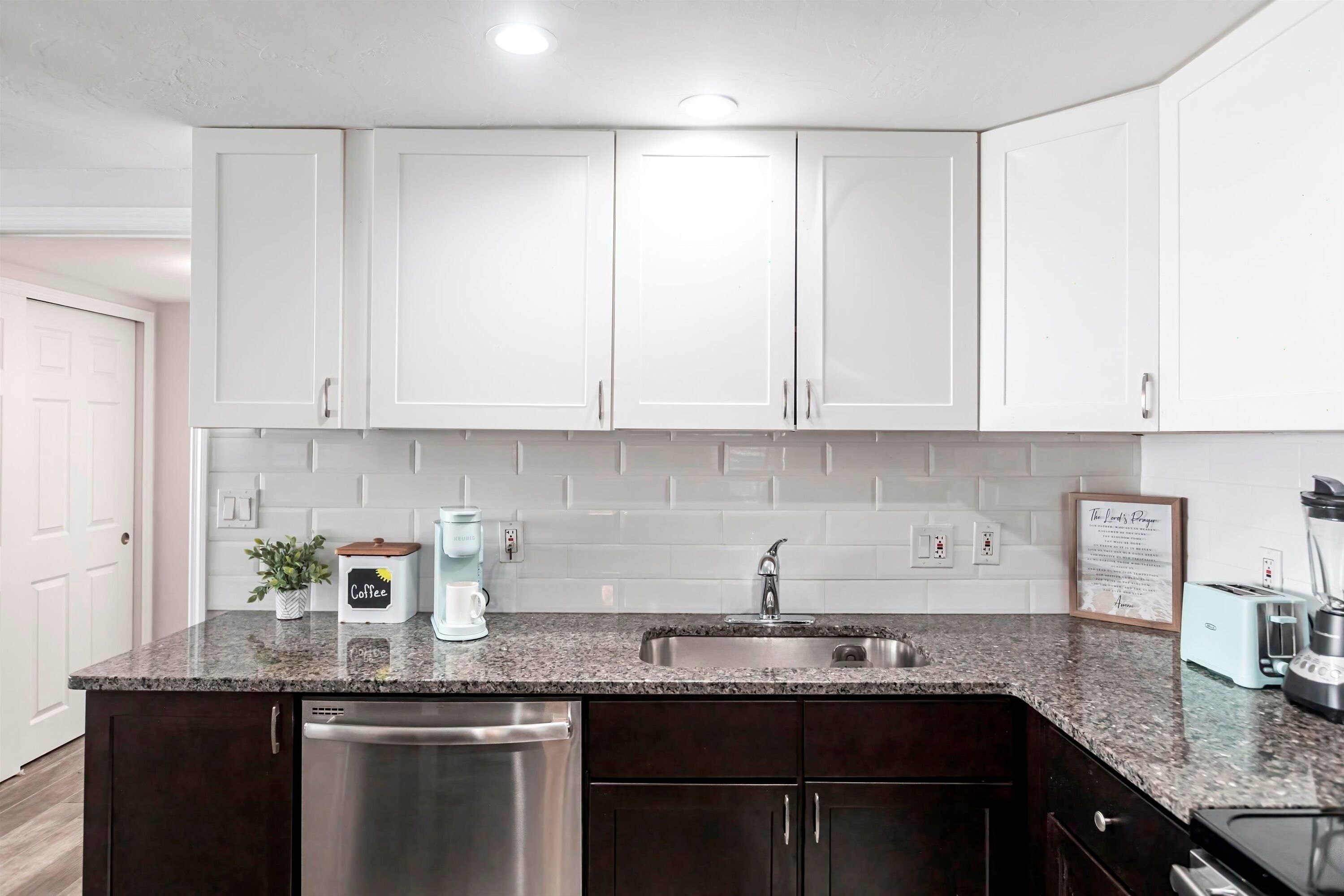 A modern kitchen with white cabinets, a granite countertop, a dishwasher, and a coffee maker.