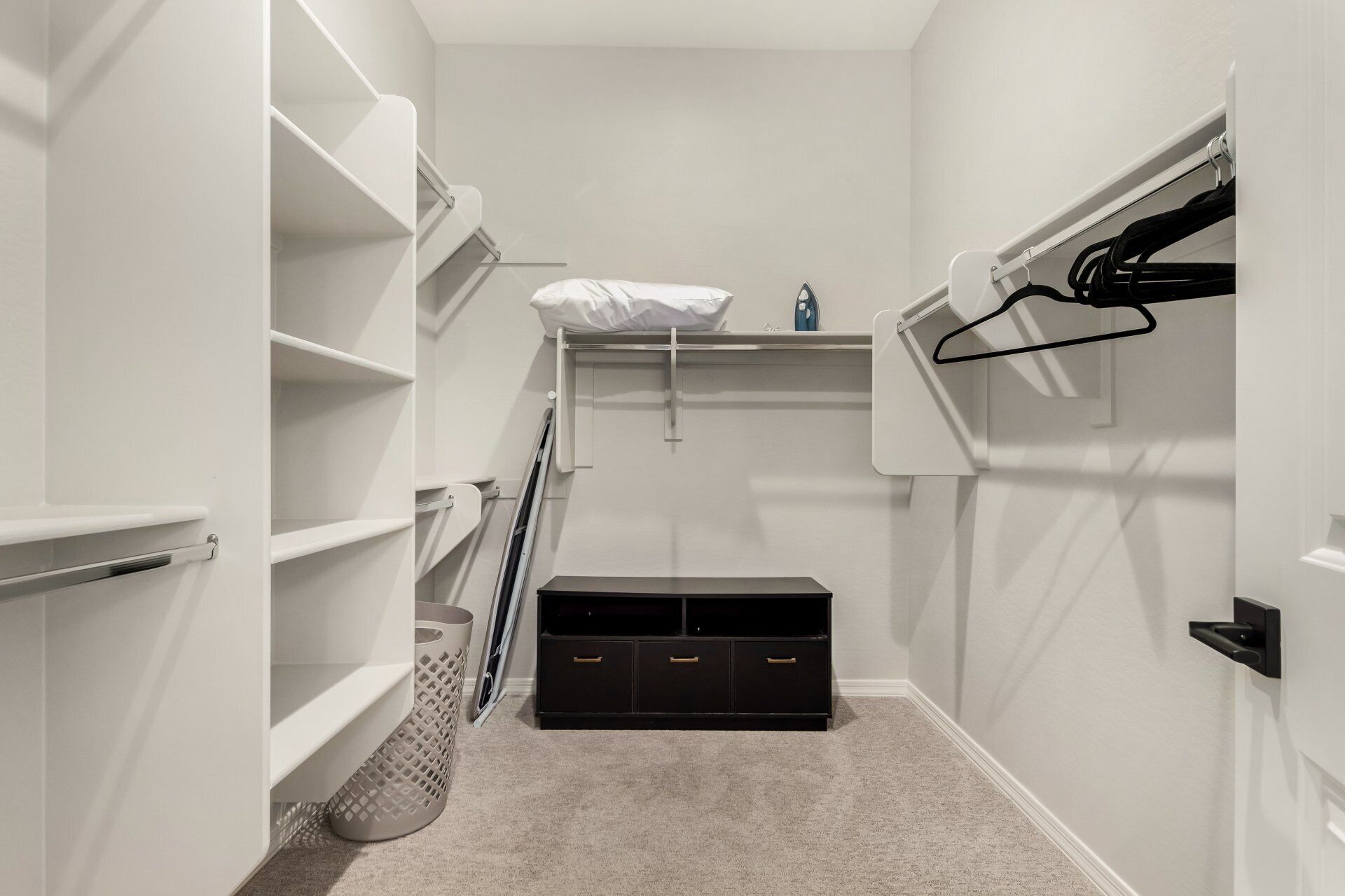 Un dressing accessible sans porte, doté d’étagères ouvertes, d’un meuble de rangement noir et d’une tringle à vêtements.