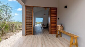A spacious corridor with wooden flooring and a bench, leading to a patio area with a view of the landscape. - Villa Kas Di Lotte, 3-bedroom villa in marvelous Coral Estate with AC, WiFi (Sint Willibrordus)