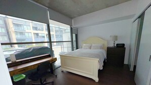A bedroom with a bed, desk, chair, and a window with a view of buildings. - Downtown Toronto  (Toronto)