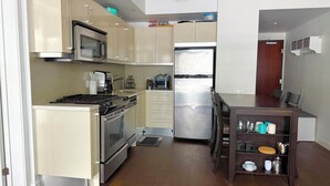 A compact kitchen with a stove, oven, microwave, and refrigerator. There is a dining table with chairs and a small shelf with dishes. - Downtown Toronto  (Toronto)