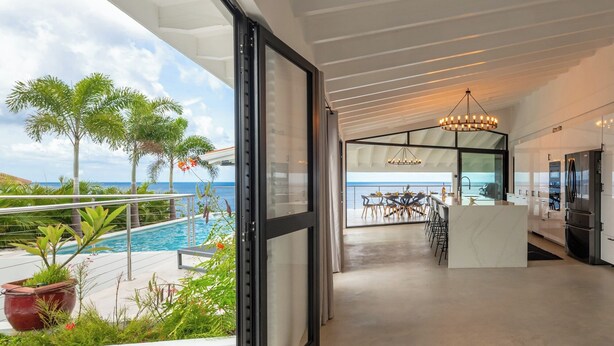 A modern kitchen with a large island, a dining area with a view of the ocean, and a pool area with tropical plants. - Villa Neshi, Spacious 5-bedroom villa in charming Cas Abou Resort with AC, WiFi (Willemstad)