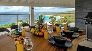 A dining table set with fruits, glasses, and a view of the ocean. - Villa Neshi, Spacious 5-bedroom villa in charming Cas Abou Resort with AC, WiFi (Willemstad)