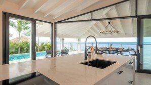 A modern kitchen with a large island, a built-in sink, and a view of the ocean. - Villa Neshi, Spacious 5-bedroom villa in charming Cas Abou Resort with AC, WiFi (Willemstad)