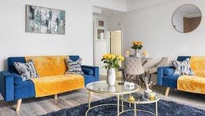 A modern living room with two blue sofas, a glass coffee table, a painting on the wall, and a round mirror. - Converted Victorian Bakery (London)