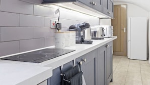A modern kitchen with grey cabinets, a white countertop, a built-in induction cooktop, a coffee maker, a toaster, and a microwave. - Converted Victorian Bakery (London)