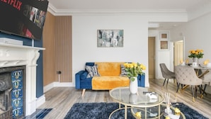 A modern living room with a blue sofa, a glass coffee table, and a fireplace. - Converted Victorian Bakery (London)