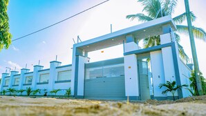 A gated entrance with a blue gate, palm trees, and a clear sky. - Villa - Sleeps 8 - Parking - Balcony (Dar es Salaam)