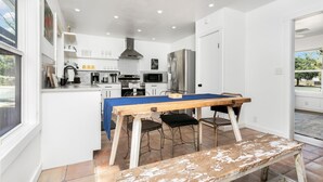 Una cocina moderna con armarios blancos, un refrigerador de acero inoxidable y una zona de comedor con mesa y taburetes de madera.