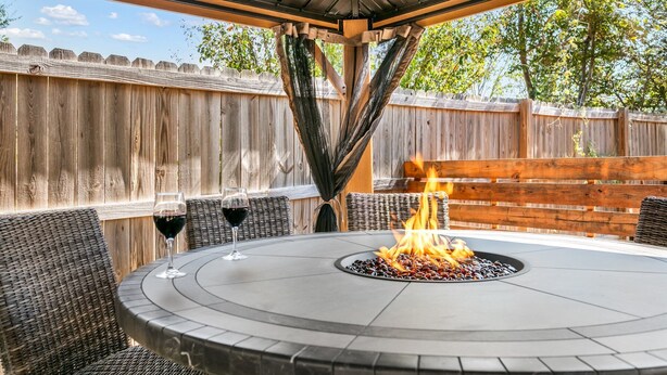 Un patio exterior circular con un hogar, mobiliario de mimbre y una valla de madera al fondo.