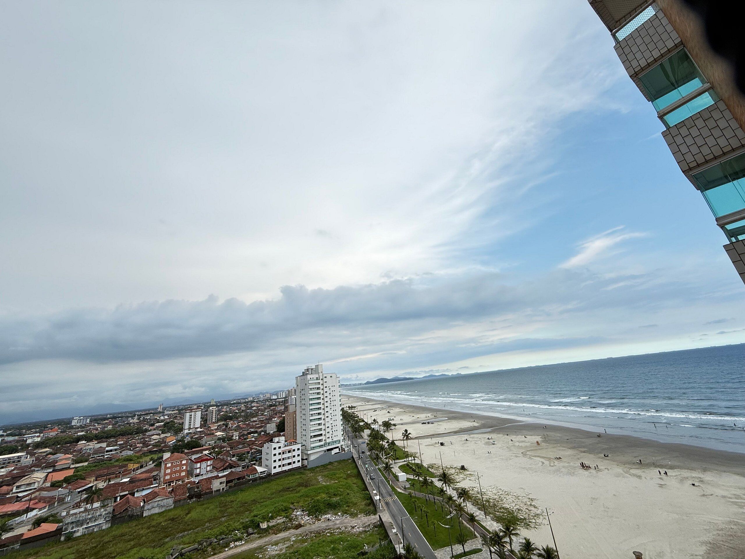 Un paisaje urbano costero con un edificio blanco destacado, una playa y una carretera bordeada de palmeras.