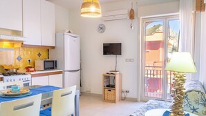 A compact living space with a kitchenette, a dining area, a TV mounted on the wall, and a balcony with a view.