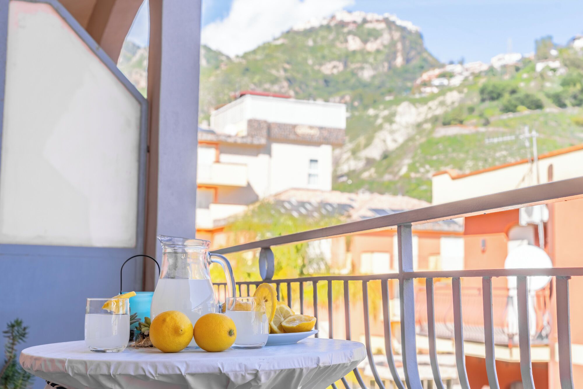 Ein Tisch mit einer Kanne, Gläsern und Orangen auf einem Balkon mit Blick auf die Berge.