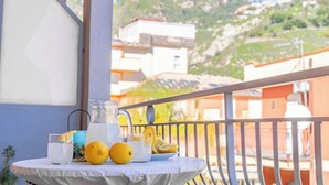 A table with a pitcher, glasses, and oranges on a balcony with a mountain view.