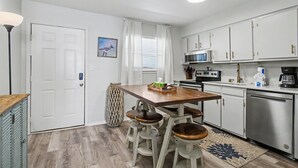 Una cocina compacta con una mesa de madera, taburetes de bar, microondas y lavavajillas.