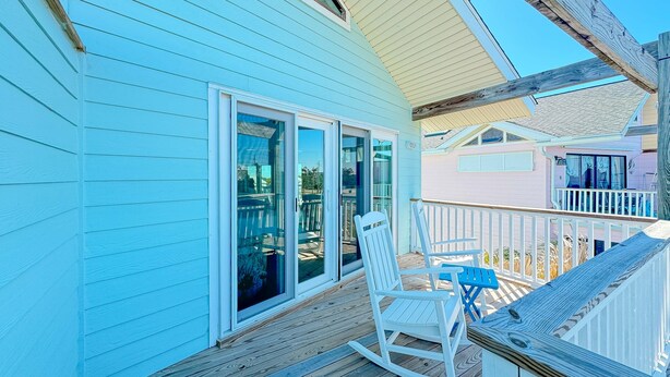 Una casa azul con terraza de madera, mecedoras blancas y una pequeña mesa.