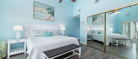 Une chambre à coucher comprenant un lit, des tables de chevet, un banc, un ventilateur de plafond et un grand miroir.