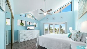 Un dormitorio con una cama grande, un ventilador de techo, un aparador y vistas al exterior.