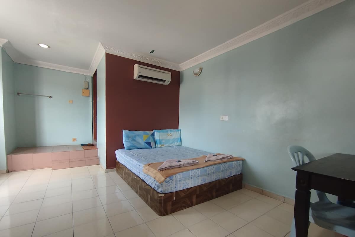 A bedroom with a bed, a desk, and an air conditioning unit.