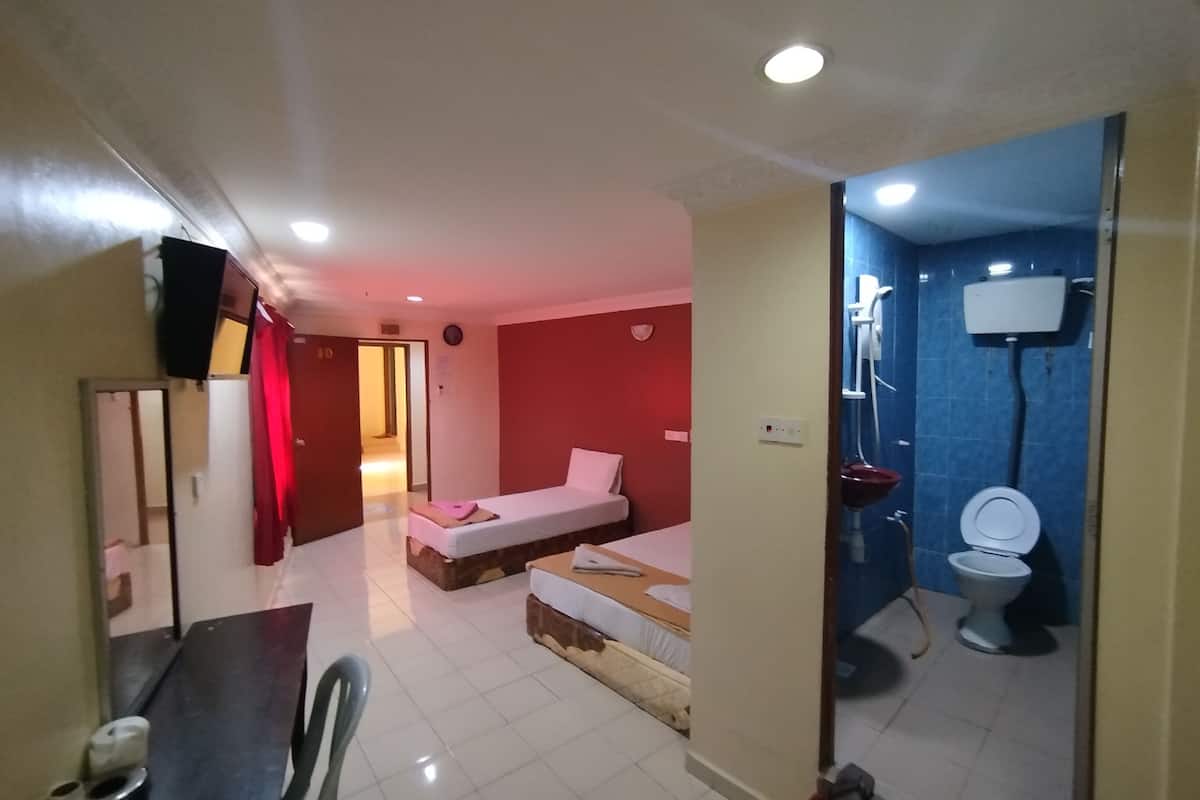 A hotel room with two beds, a small table with chairs, a bathroom with a toilet and shower, and a red wall.