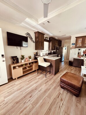 A modern kitchen with wooden cabinets, a built-in island, and a flat-screen TV mounted on the wall.