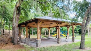 A covered pavilion with picnic tables and benches, surrounded by trees and a playground with a slide. - Get 10% off on weekly stay or 15% on monthly stay. Fully equipped cabin. CR. Fl (Crystal River)