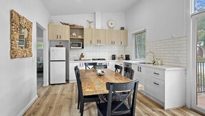 A modern kitchen with white cabinets, a wooden dining table, and a built-in microwave. - The Purple Hen Hideaway Ramada (Cowes)