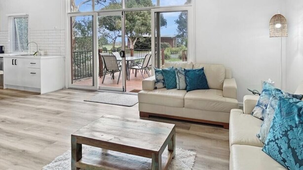 A modern living room with a sofa, a coffee table, and a dining area with chairs. - The Purple Hen Hideaway Ramada (Cowes)