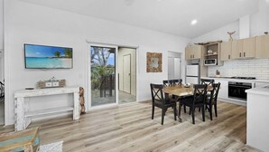 A modern kitchen with white cabinets, a dining area with a wooden table and chairs, and a sliding glass door leading to a balcony. - The Purple Hen Hideaway Ramada (Cowes)