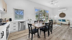 A modern kitchen with white cabinetry, a dining table with chairs, a dishwasher, and a large window. - The Purple Hen Hideaway Ramada (Cowes)