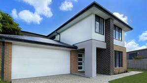 Een modern huis met twee verdiepingen, een witte garageklep, een bakstenen schoorsteen en een verzorgd gazon.