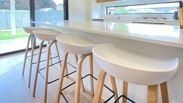 Een moderne keuken met een groot eiland, barkrukken en uitzicht op de buitenruimte.