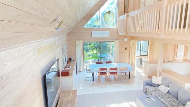 A modern interior with a wooden ceiling, a dining area with a table and chairs, a sofa, and a TV mounted on the wall. - Surfs Up on Surf Parade (Inverloch)